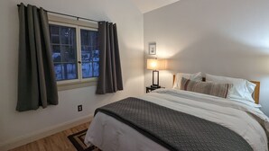 Ein Schlafzimmer mit einem Bett, einem Nachttisch, einer Lampe und einem Fenster mit Vorhängen.