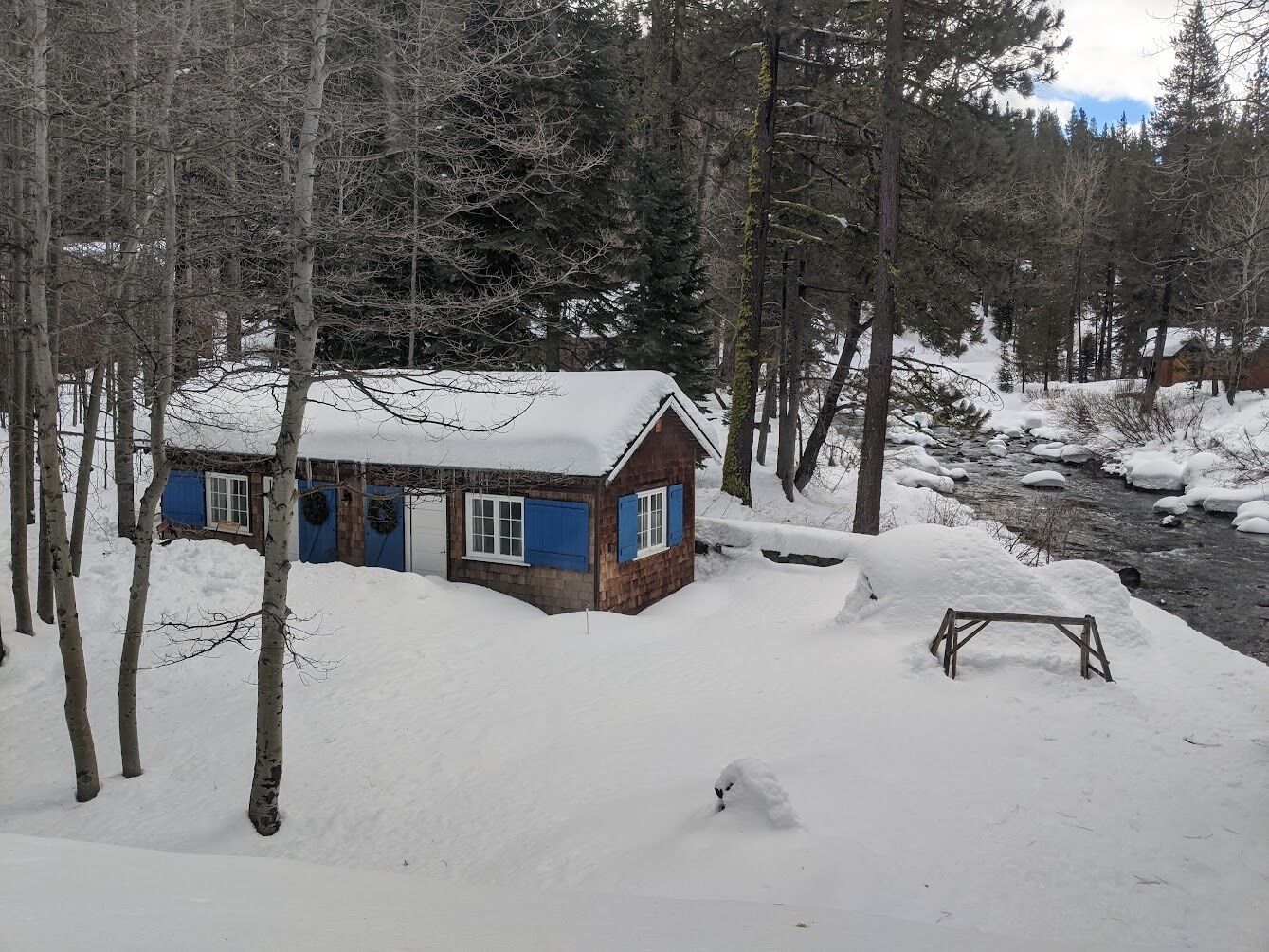 Une cabane dont le toit est recouvert de neige, entourée d’arbres et bordée d’une épaisse couche de neige.