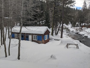Une cabane dont le toit est recouvert de neige, entourée d’arbres et bordée d’une épaisse couche de neige.
