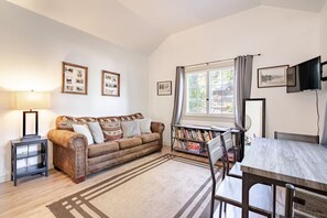 Un salon chaleureux avec un canapé, une table basse, une bibliothèque et un téléviseur fixé au mur.