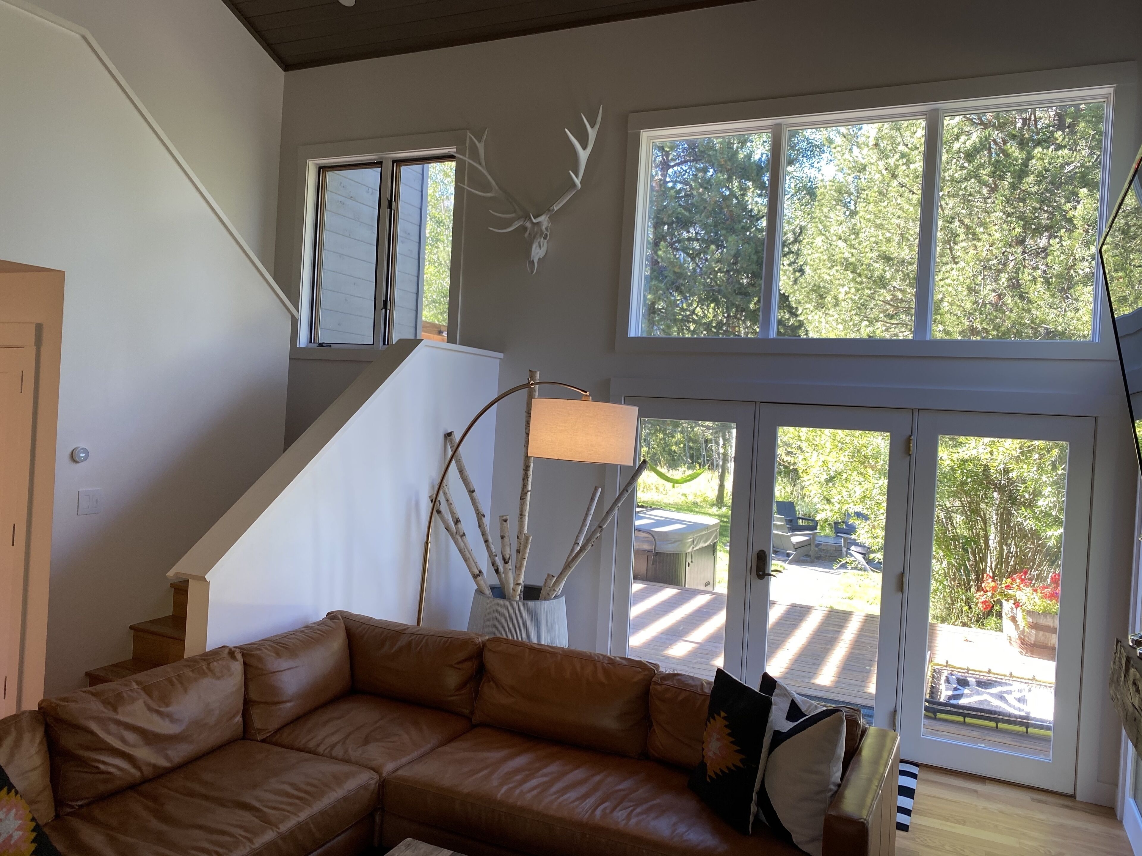 A spacious living room with a brown leather sofa, a large window with a deer skull decoration, and a staircase leading to an upper level.