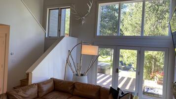 A spacious living room with a brown leather sofa, a large window with a deer skull decoration, and a staircase leading to an upper level.