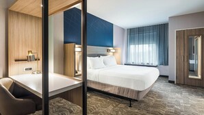 Habitación de hotel con cama, escritorio, silla, un espejo grande y ventana con cortinas.