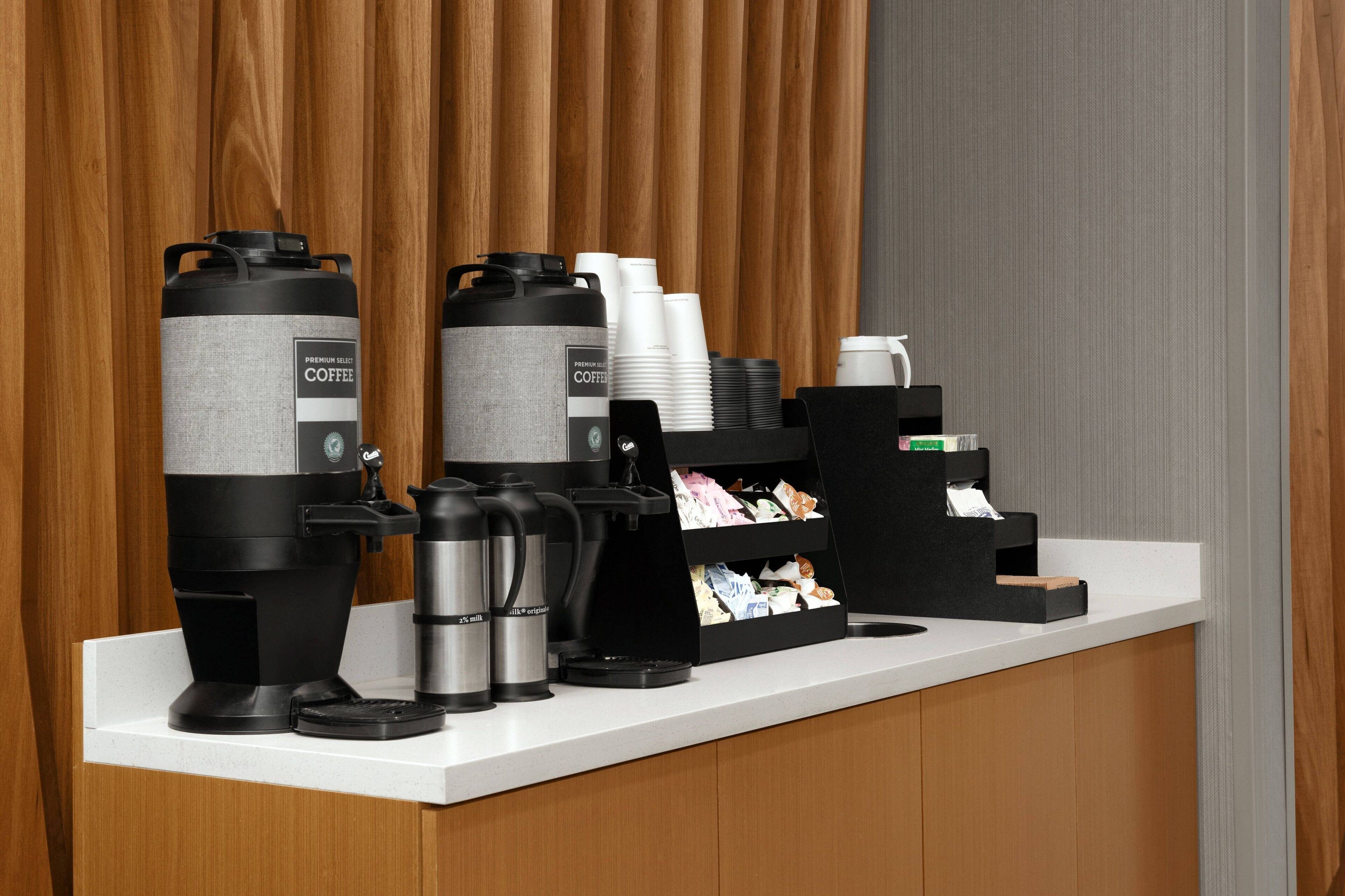 Een koffiehoek met meerdere koffiezetapparaten, wegwerpbekers en een koffieautomaat.