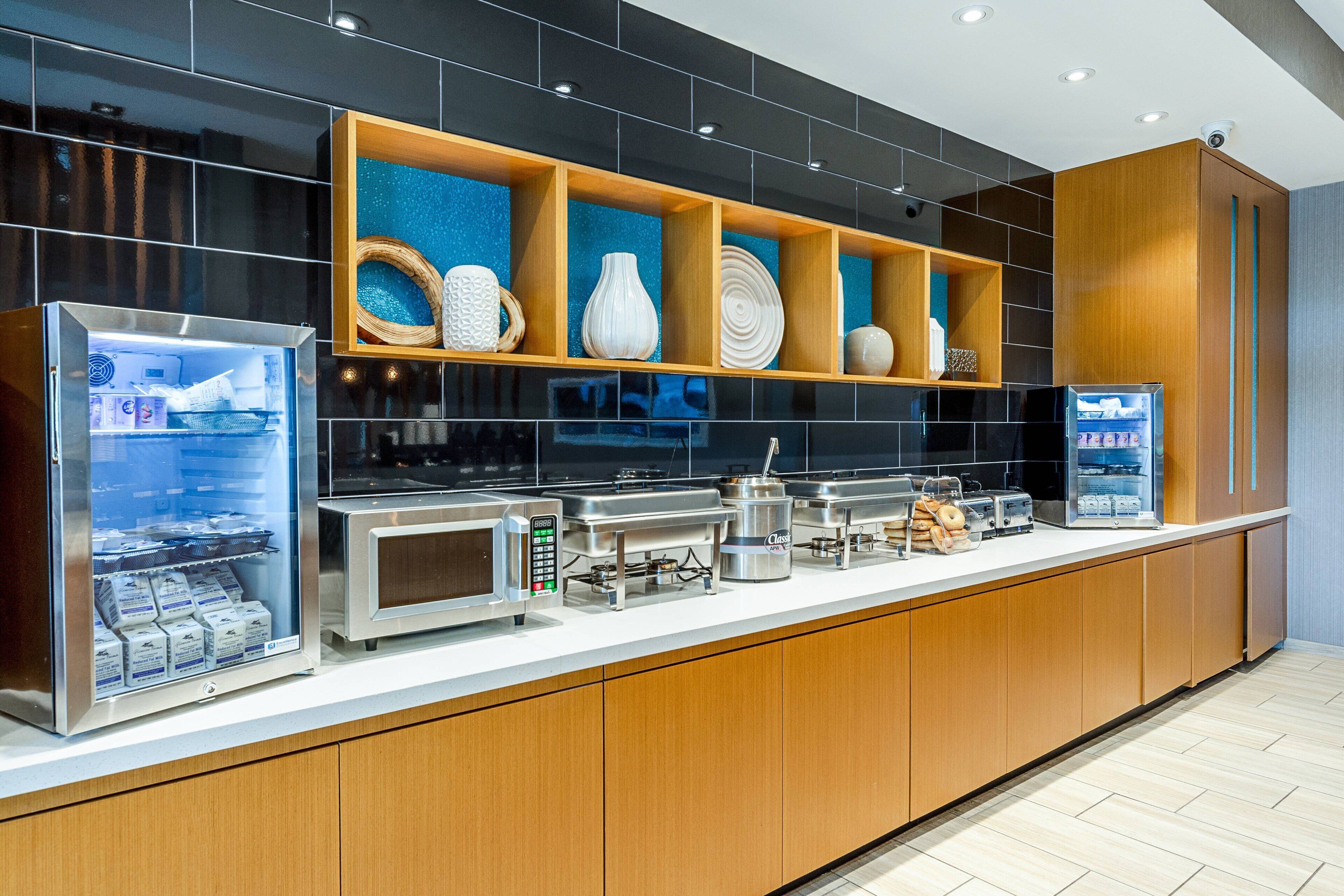 Una barra de desayuno moderna con un mostrador refrigerado, una máquina de café y diversas opciones para el desayuno.