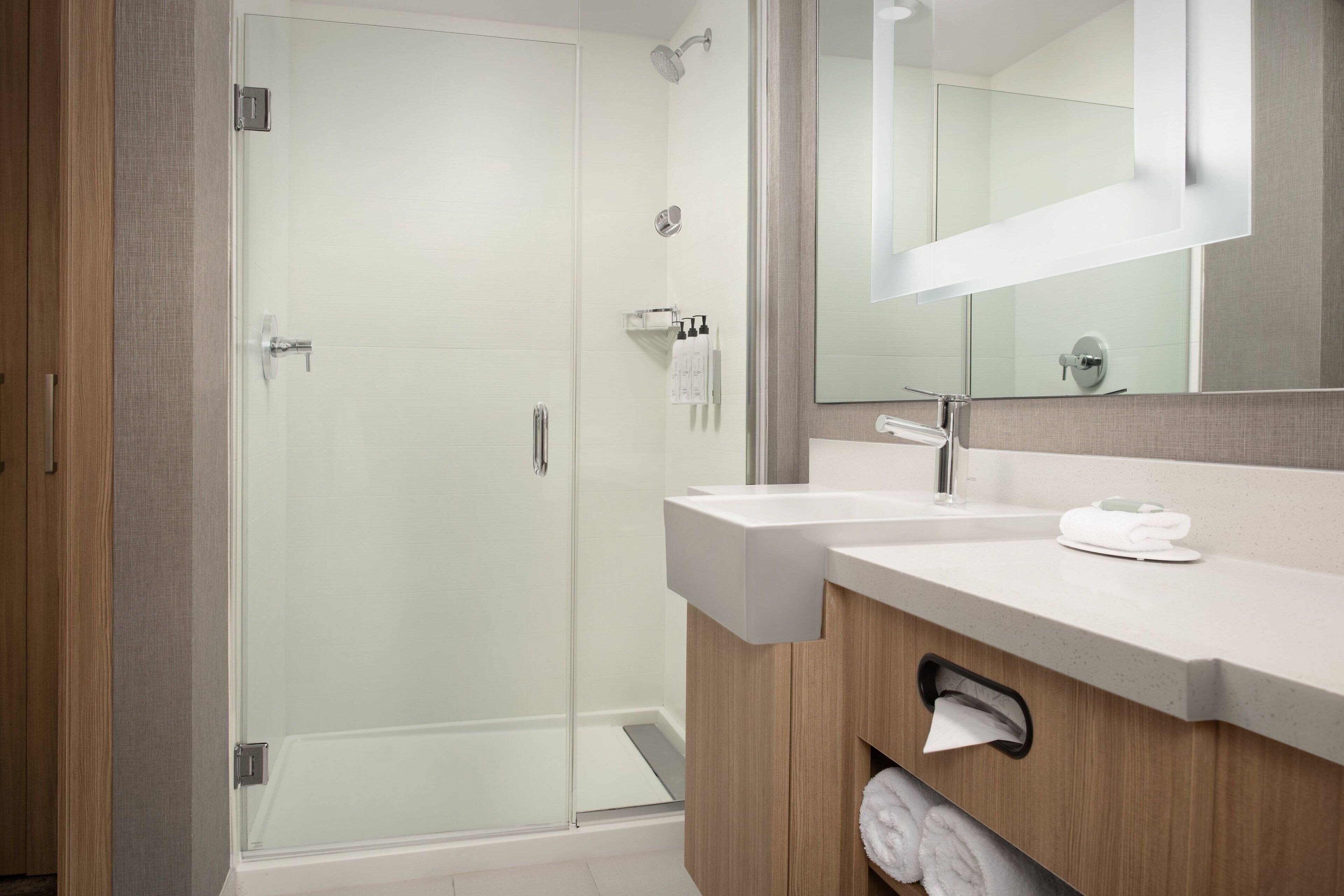 A modern bathroom with a glass shower enclosure, a wooden vanity with a sink, and a large mirror above the vanity.