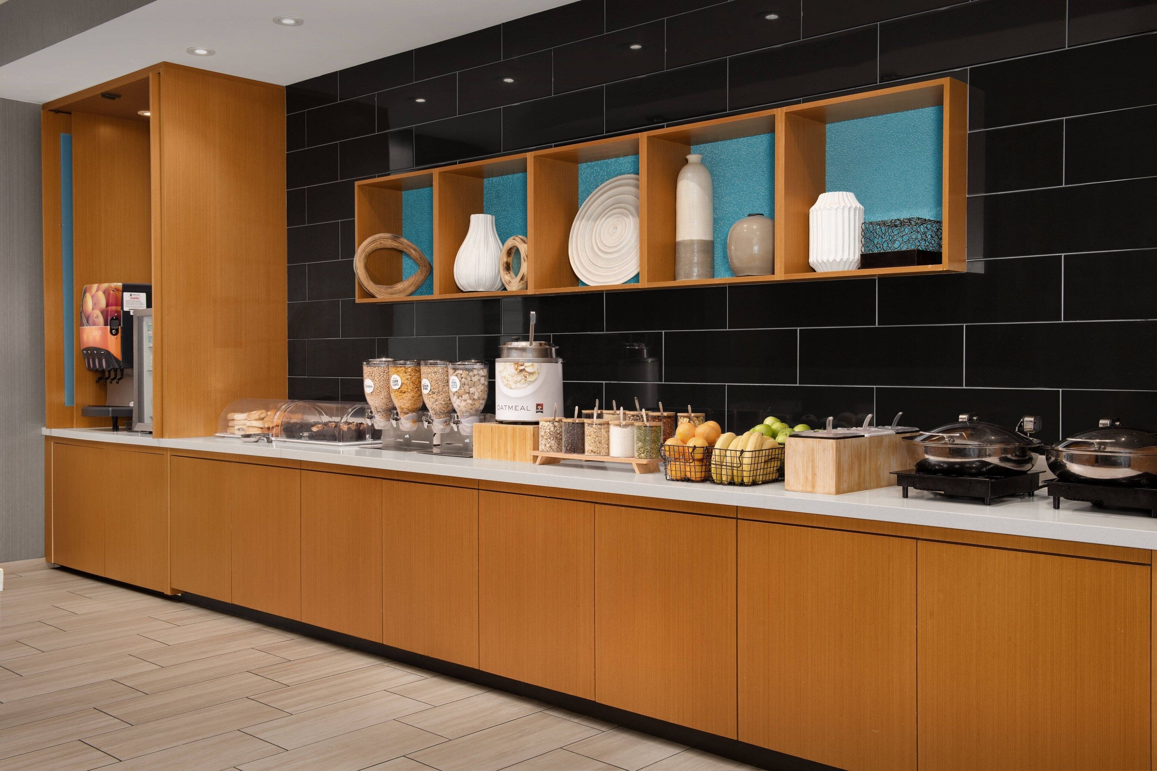 Une cuisine moderne avec des meubles en bois, un plan de travail sur lequel sont disposés divers aliments, et un dosseret noir en carreaux.