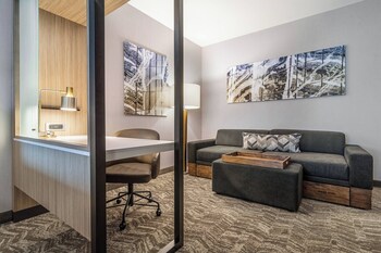 A swimming pool with lounge chairs and a stone wall, surrounded by a building with large windows and a blue exterior. at SpringHill Suites by Marriott Charleston Airport & Convention Center