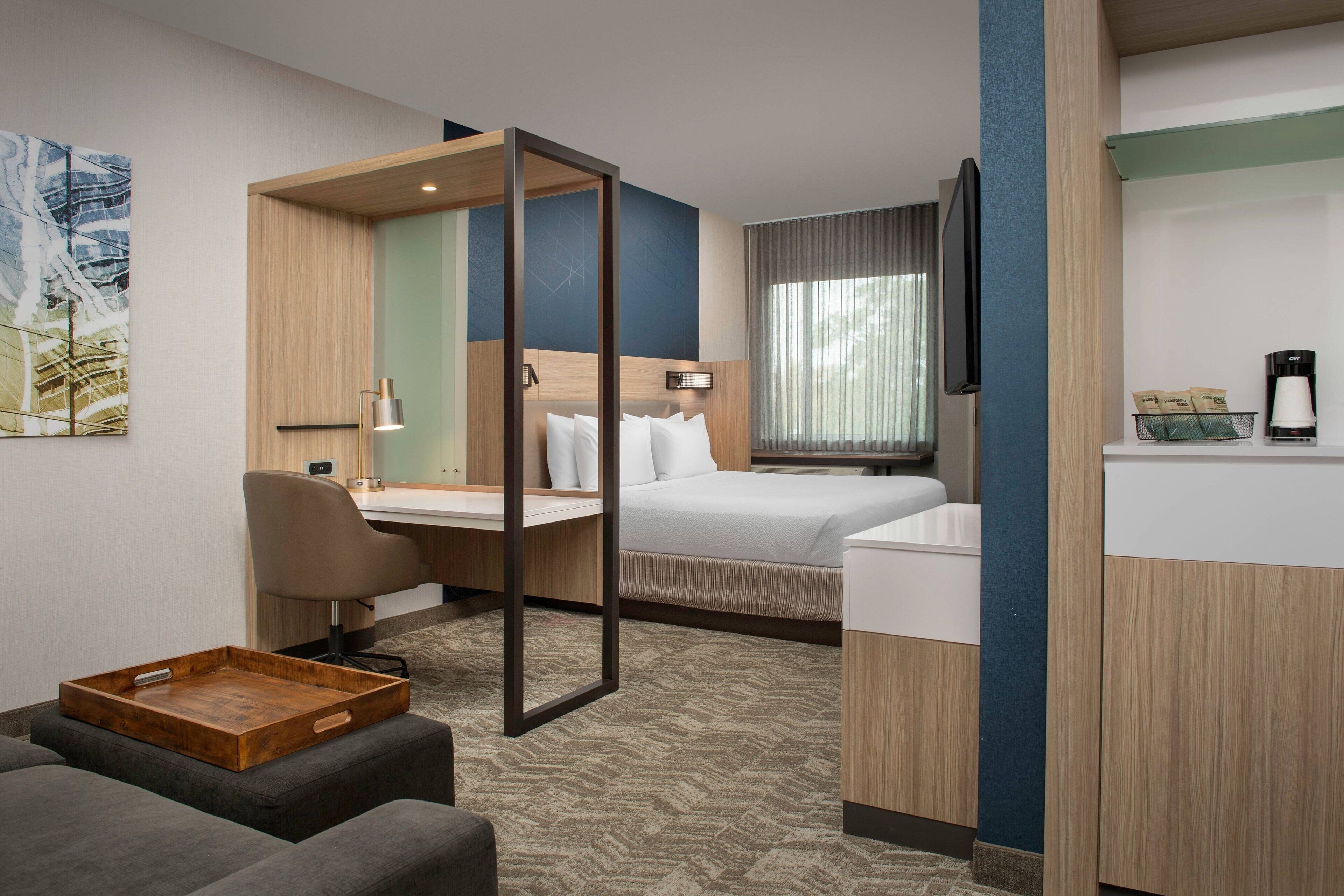 A hotel room with a bed, desk, chair, and a small seating area.