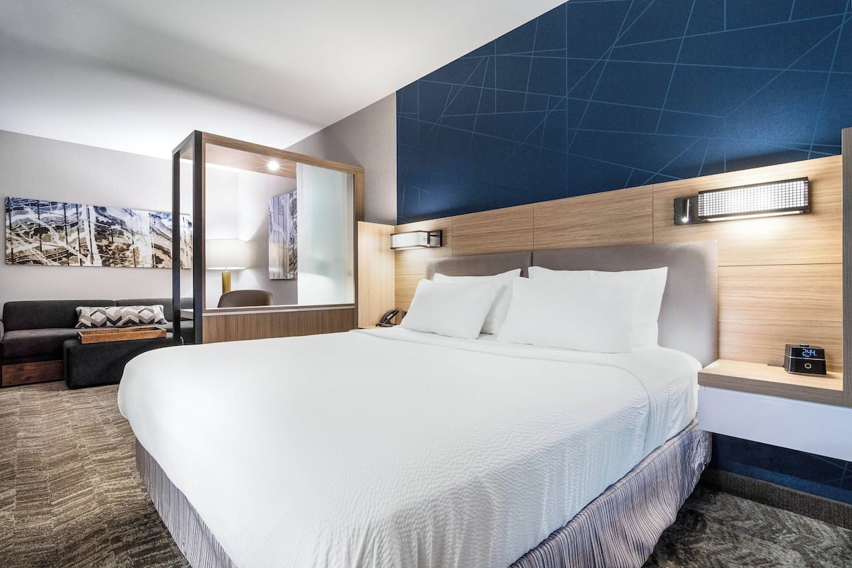Een moderne hotelkamer met een groot bed, een houten hoofdbord, een nachtkastje, een spiegel en een wandlamp.