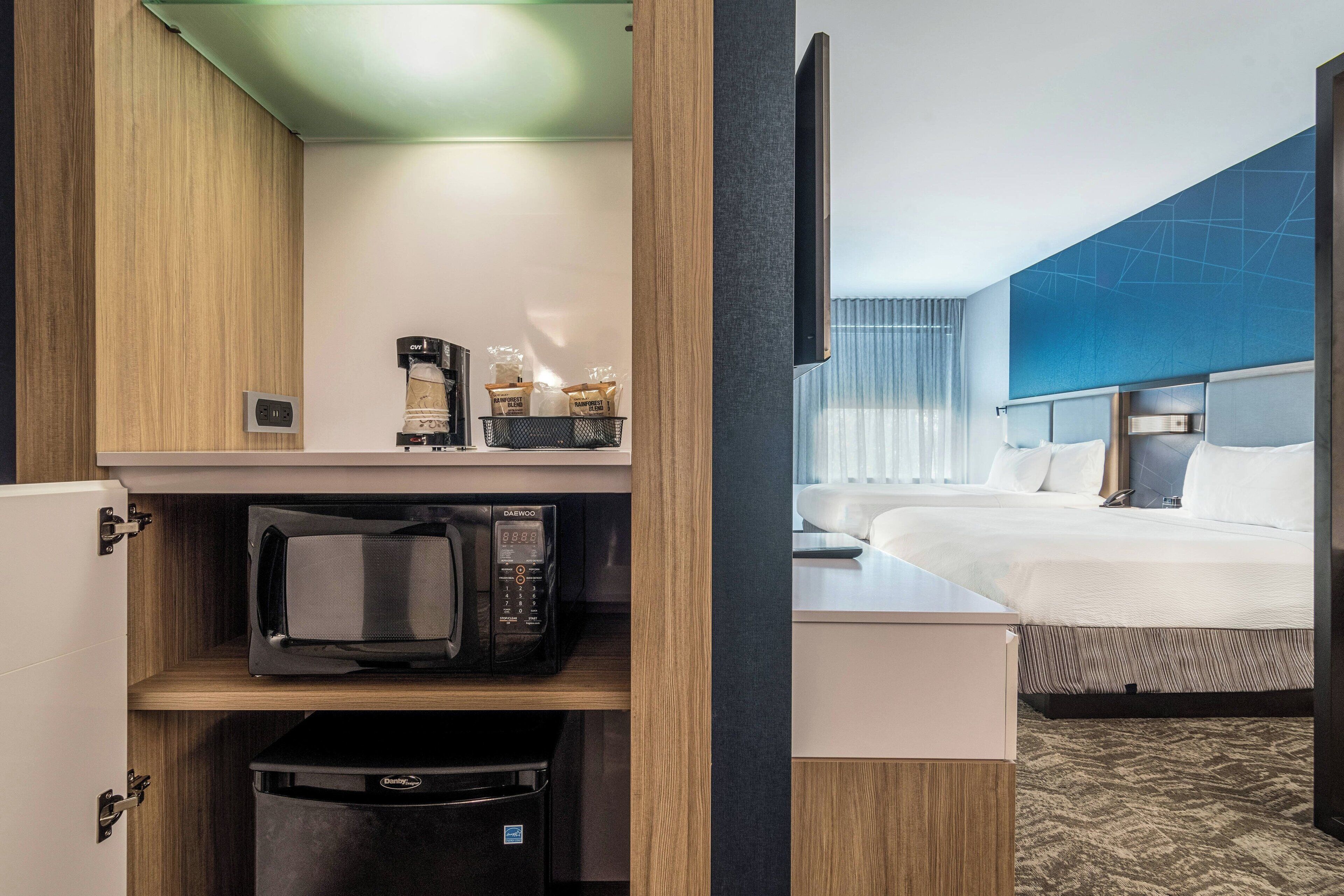 A hotel room with a bed, a TV mounted on the wall, a microwave, and a coffee maker on a shelf.