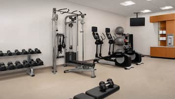 Een sportschool met trainingsapparatuur, gewichten en een bank.