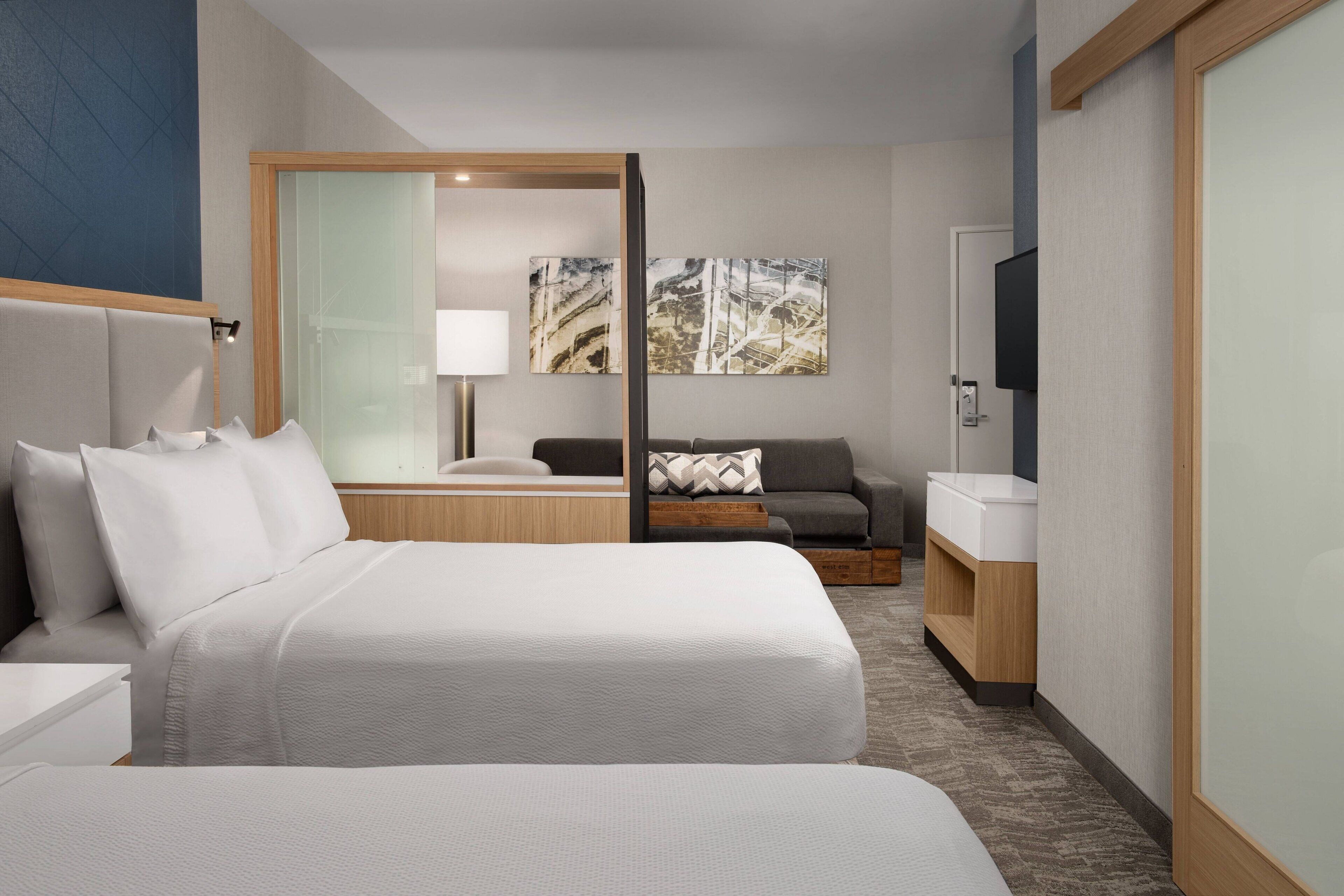 A hotel room with two beds, a sofa, a TV, and a mirror.