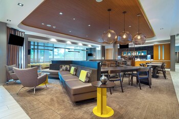 A modern hotel room with a desk, chair, sofa, ottoman, and two abstract paintings on the wall. at SpringHill Suites by Marriott Charleston Airport & Convention Center