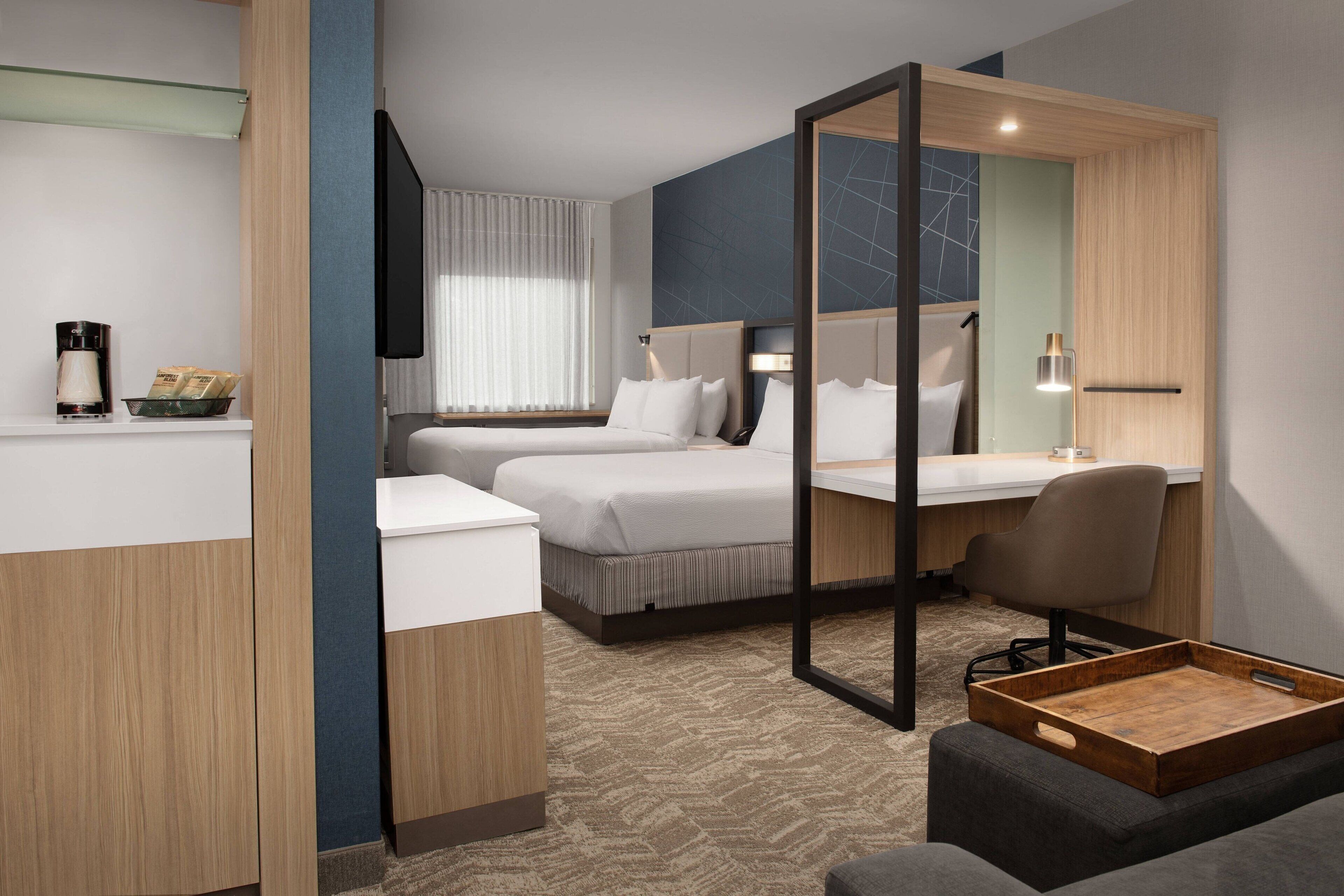 A modern hotel room with a bed, a desk, a chair, and a small table.