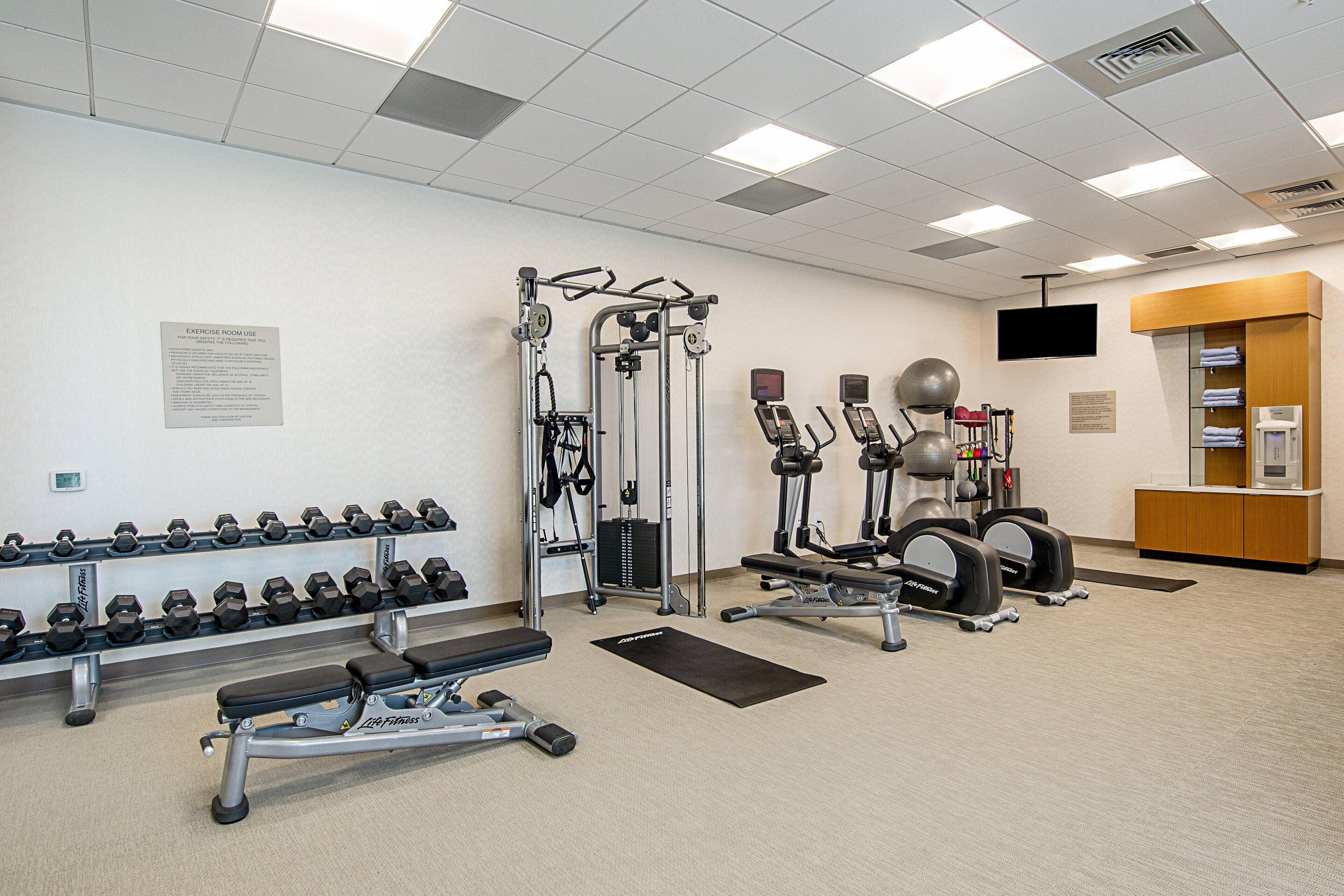 A gym with exercise equipment, dumbbells, and a bench.