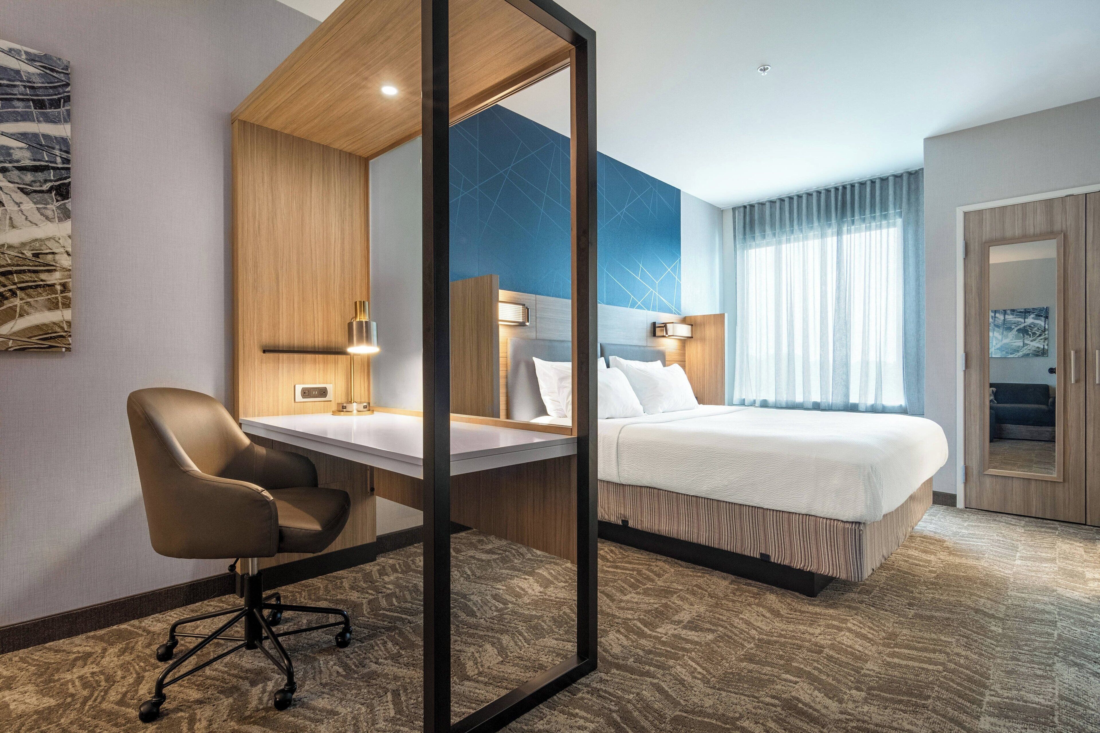 A hotel room with a bed, a desk, a chair, and a large mirror.