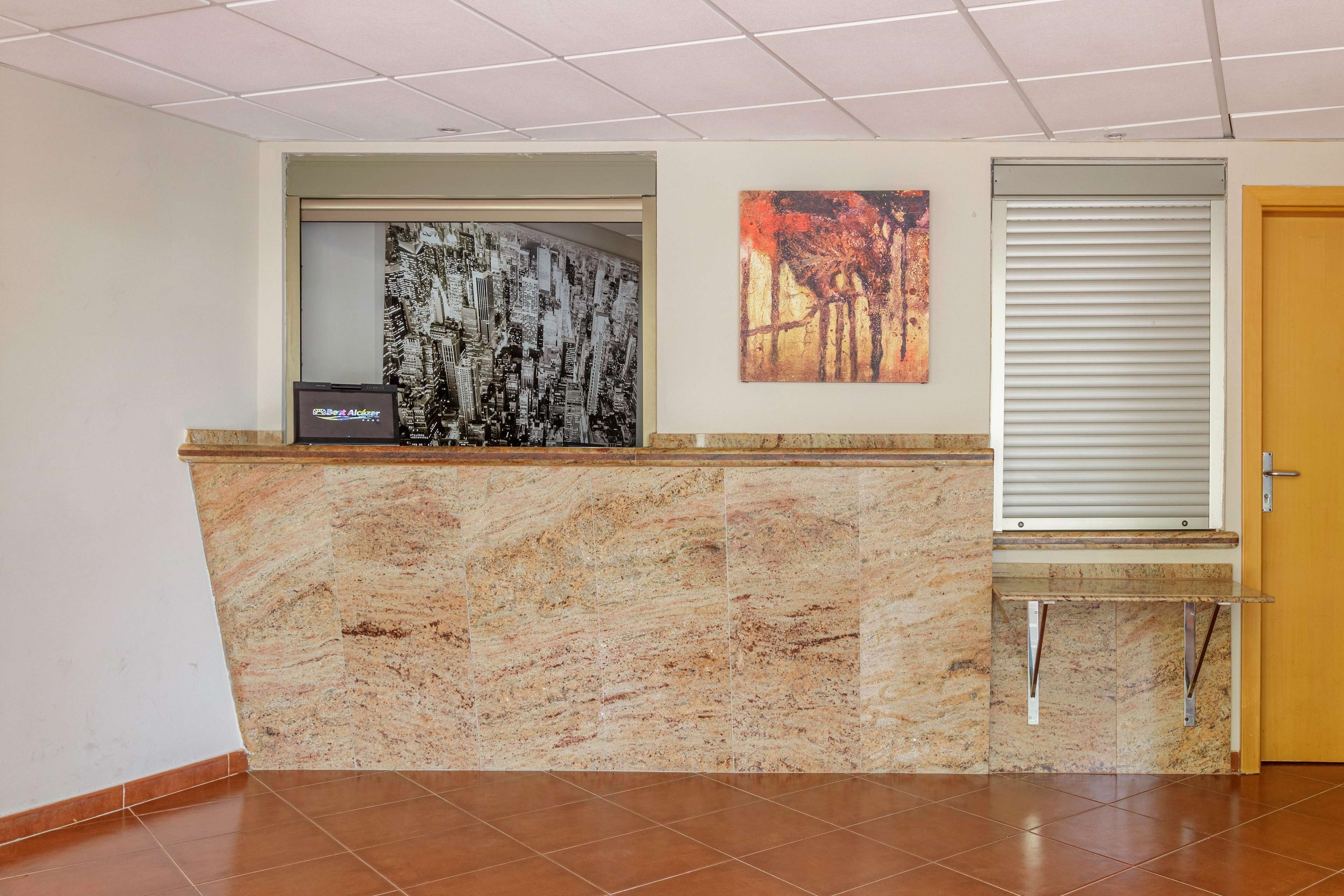 A reception area with a marble counter, a cityscape artwork, a forest painting, and a closed door.