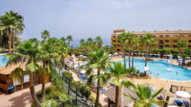 Un resort con varias piscinas, palmeras y un edificio con balcones.