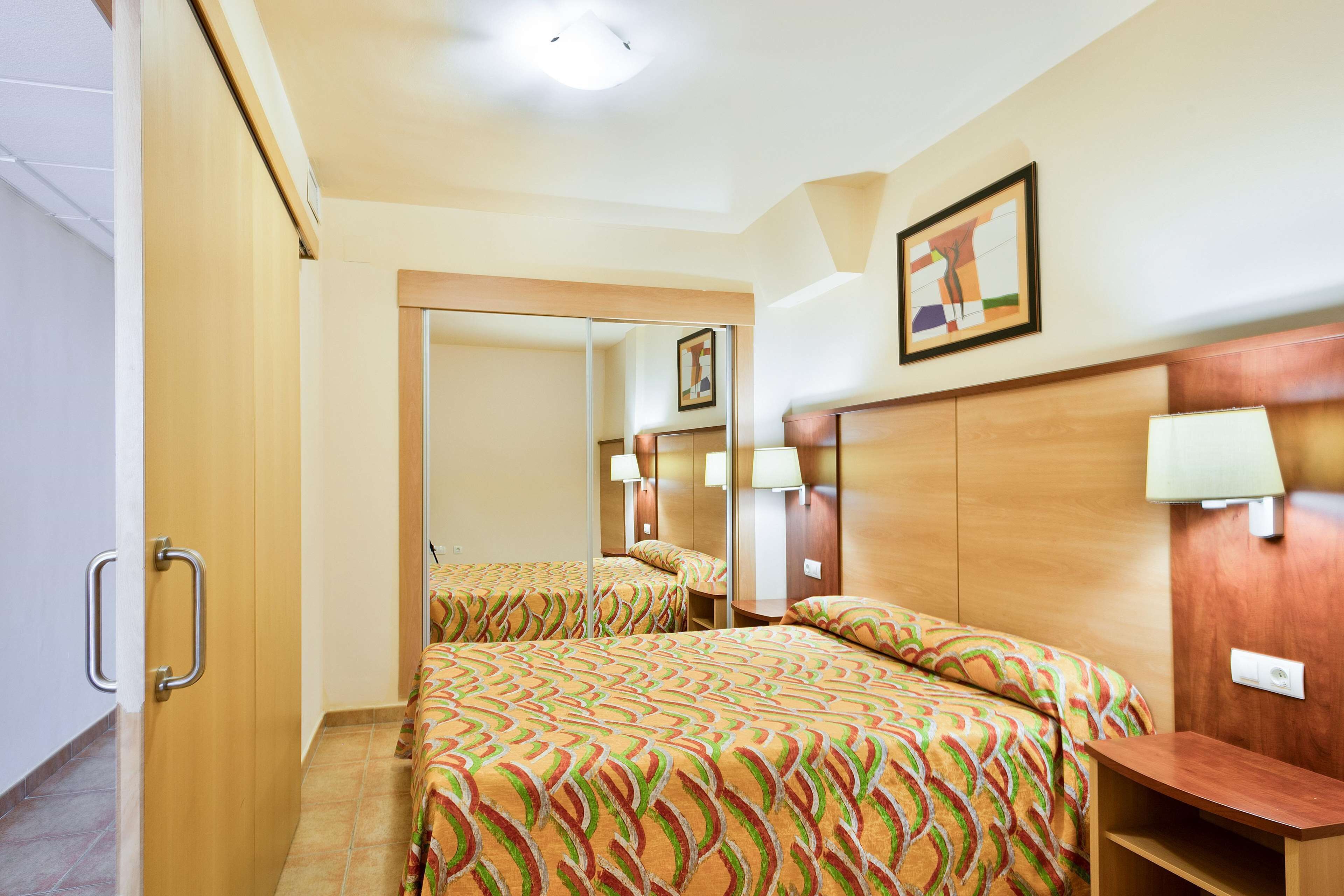 A hotel room with a bed, bedside tables, a mirror, and a door with a handle.
