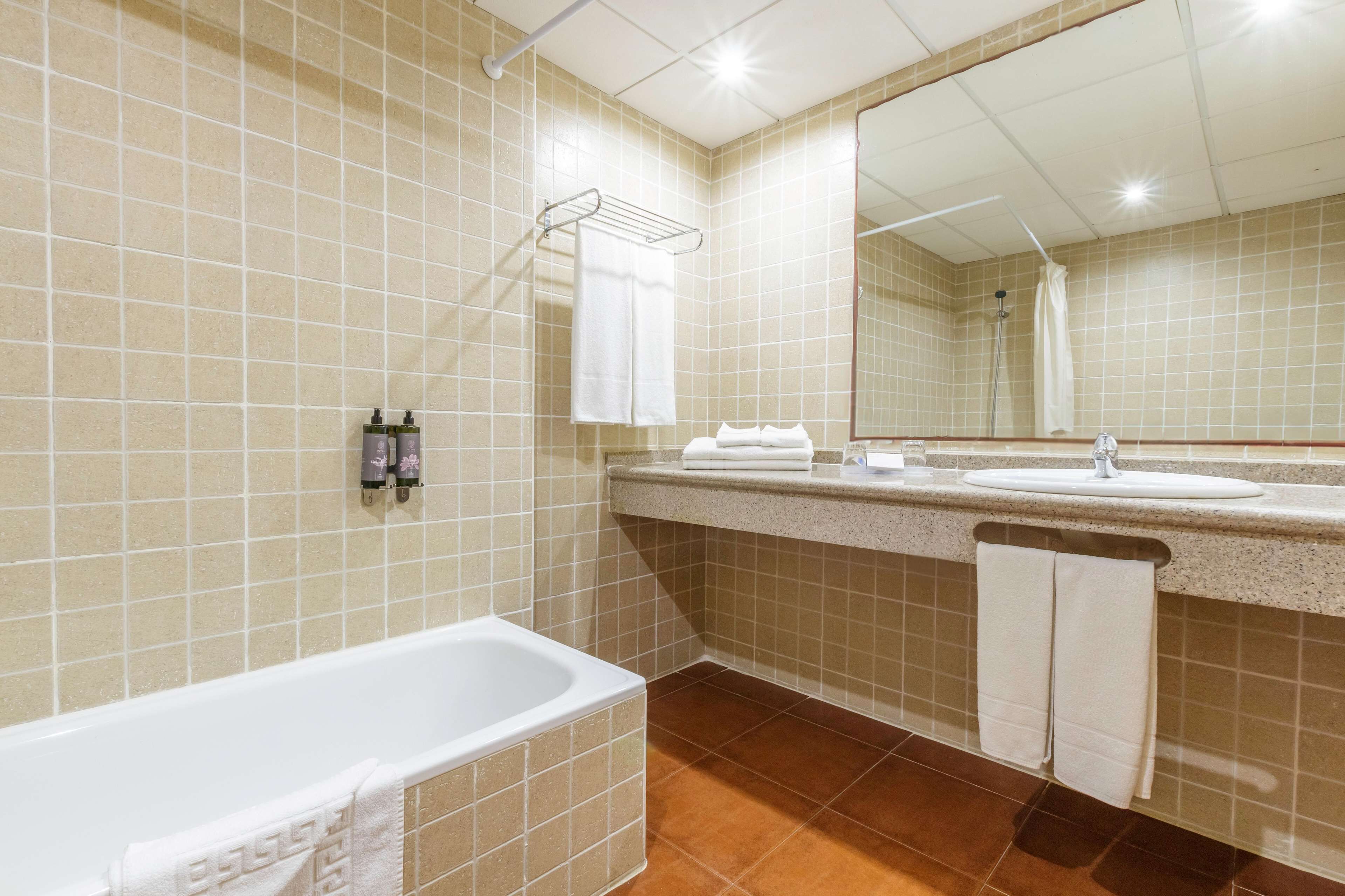 Ein Badezimmer mit einer Badewanne, einem Waschbecken und einer Dusche. Handtücher hängen an einem Halter und über dem Waschbecken hängt ein Spiegel.