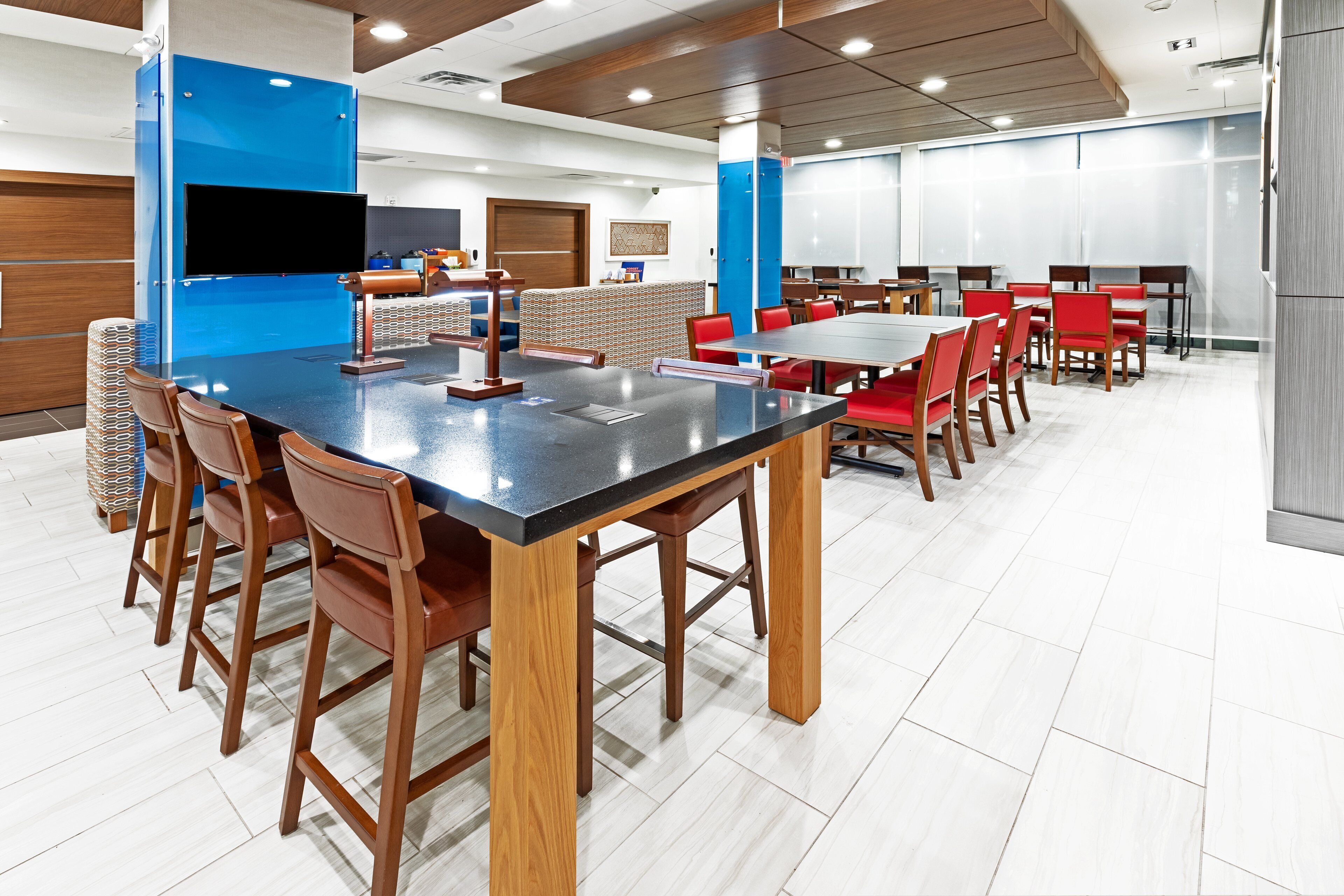 A modern dining area with a long table and red chairs, a blue accent wall, and a large window.