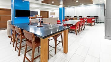 A modern dining area with a long table and red chairs, a blue accent wall, and a large window.