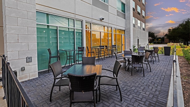 An outdoor seating area with tables and chairs, a brick floor, and a building with large windows and a glass door. - Holiday Inn Express & Suites Stafford NW - Sugar Land by IHG (Stafford)