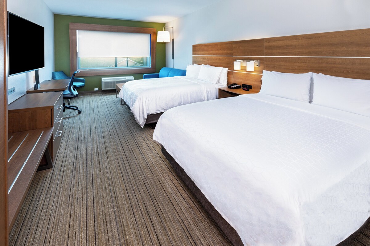 Quarto de hotel com duas camas, uma mesa, televisão e janela com vista.