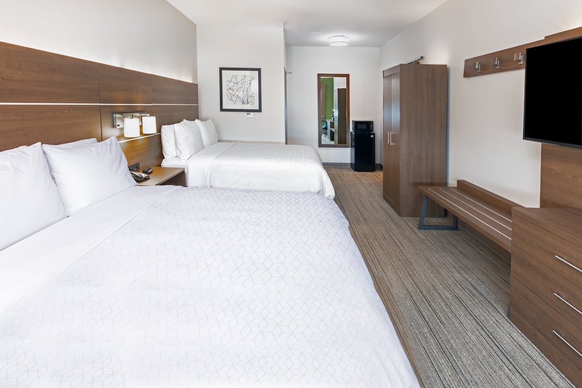 Ein Hotelzimmer mit zwei Betten, einem Schreibtisch, einem Stuhl, einem Fernseher und einem Kleiderschrank.