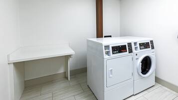 A laundry room with a white washing machine and dryer, a wooden column, and a white bench.