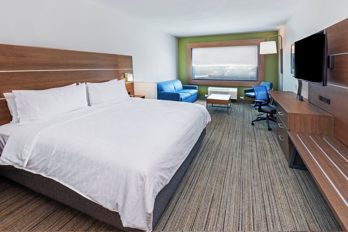 Quarto de hotel com uma cama grande, uma mesa com cadeira, uma televisão e uma janela com vista.