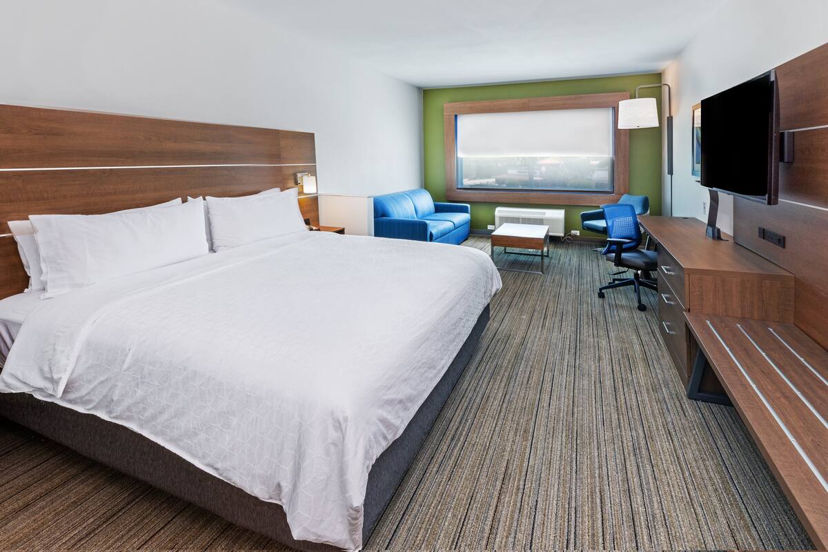 Ein Hotelzimmer mit einem großen Bett, einem Schreibtisch mit Stuhl, einem Fernseher und einem Fenster mit Ausblick.