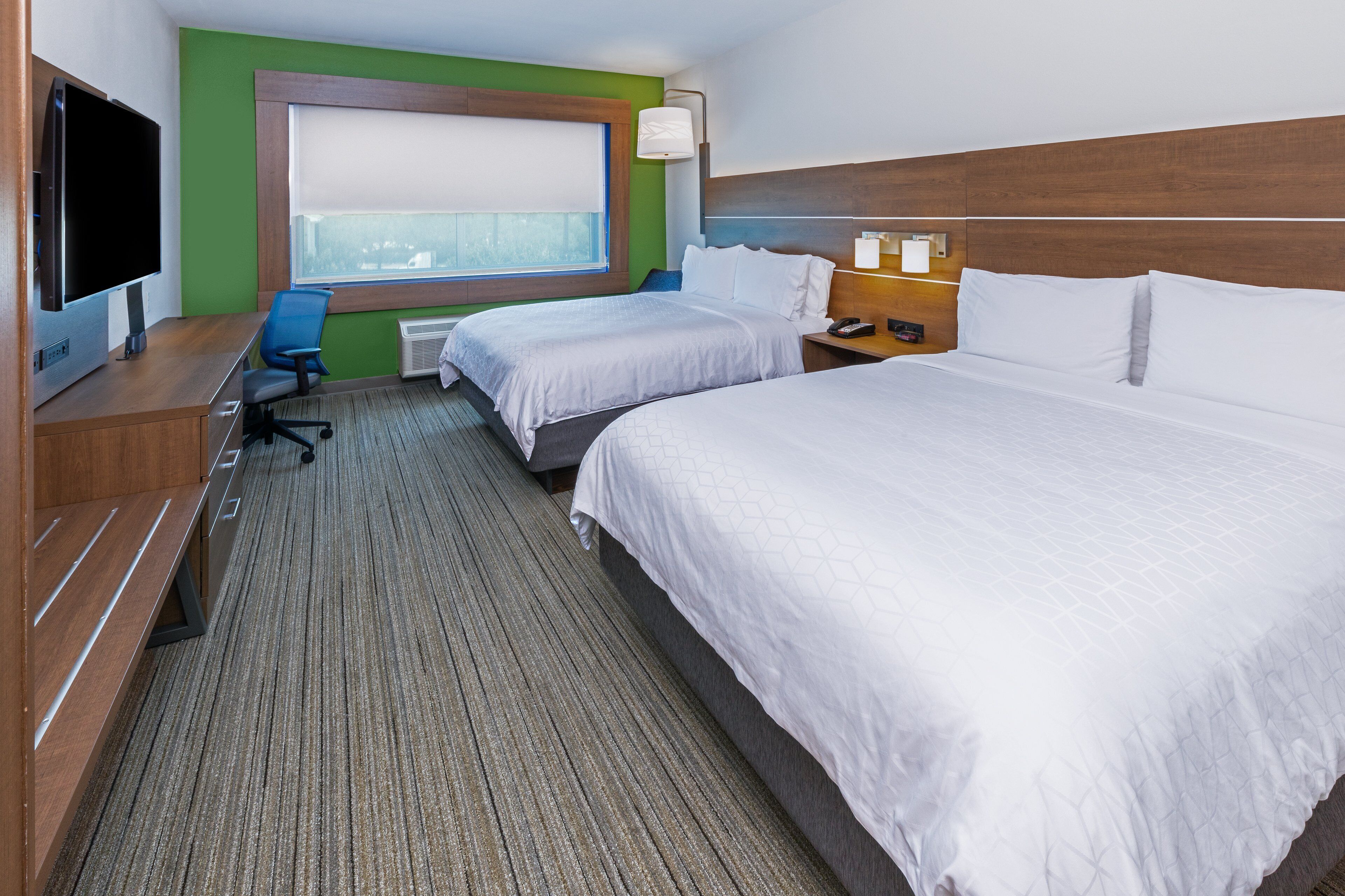 A hotel room with two beds, a desk with a computer, a TV, and a window with blinds.