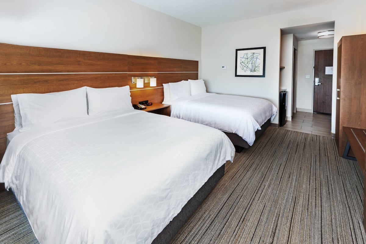 Une chambre d’hôtel avec deux lits, une tête de lit en bois, une table de chevet avec un téléphone et un tableau encadré au mur.