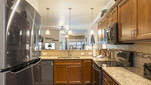 Une cuisine moderne dotée d’appareils électroménagers en acier inoxydable, de meubles en bois, de plans de travail en granit et de luminaires suspendus.