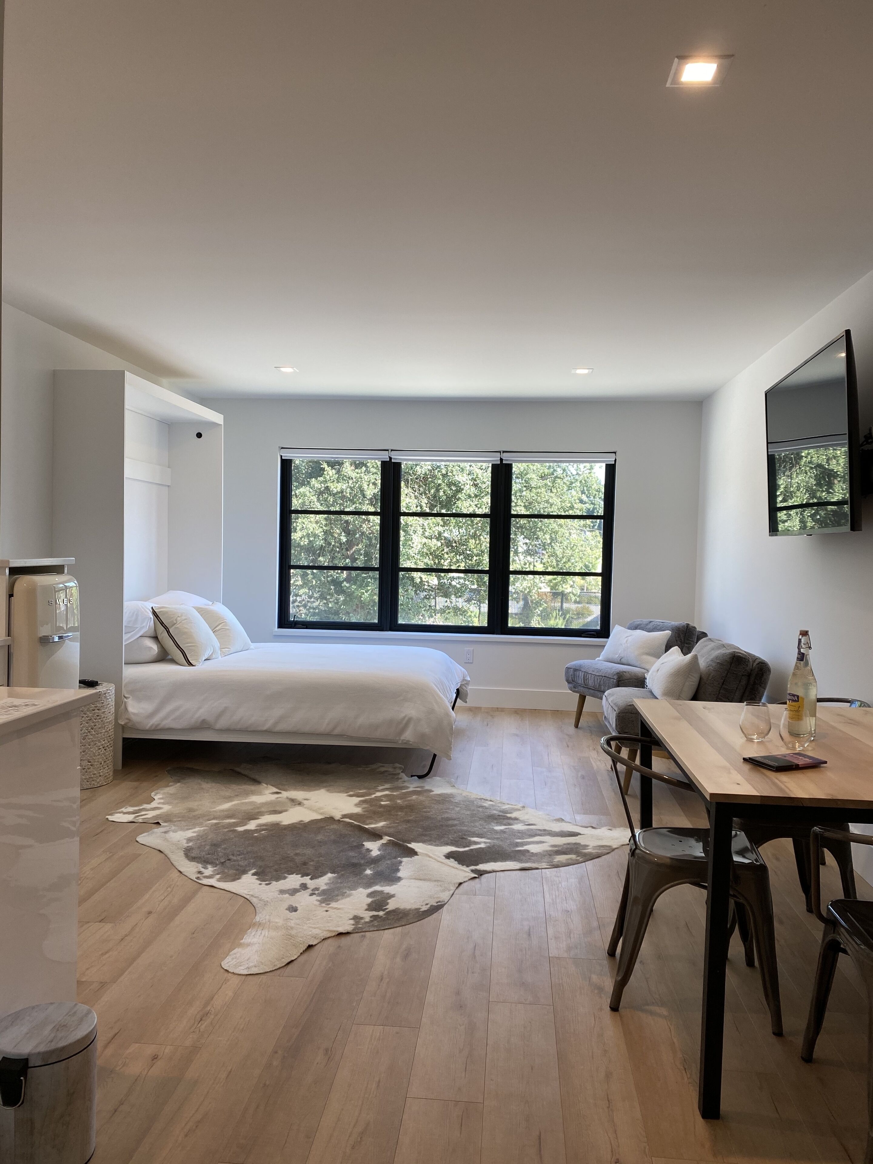 A modern bedroom with a large window, a bed, a desk, and a cowhide rug.