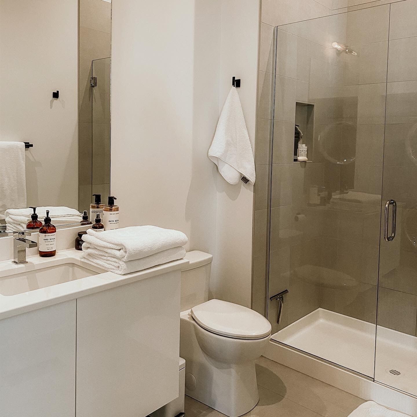 A modern bathroom with a glass shower enclosure, a white toilet, and a vanity with toiletries.