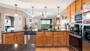 Una cucina moderna con mobili in legno, un piano di lavoro nero, elettrodomestici in acciaio inossidabile e illuminazione a sospensione.