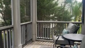 Un espace extérieur abrité, doté d’une table et de chaises, d’une rambarde et offrant une vue sur les arbres et les bâtiments.