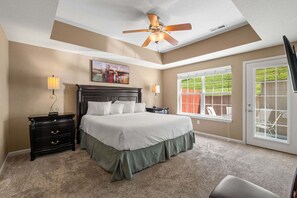 A bedroom with a bed, nightstands, a ceiling fan, a window with a view, and a door.