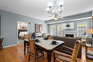 A dining area with a table set for four, surrounded by wicker chairs, a chandelier, and a fireplace.