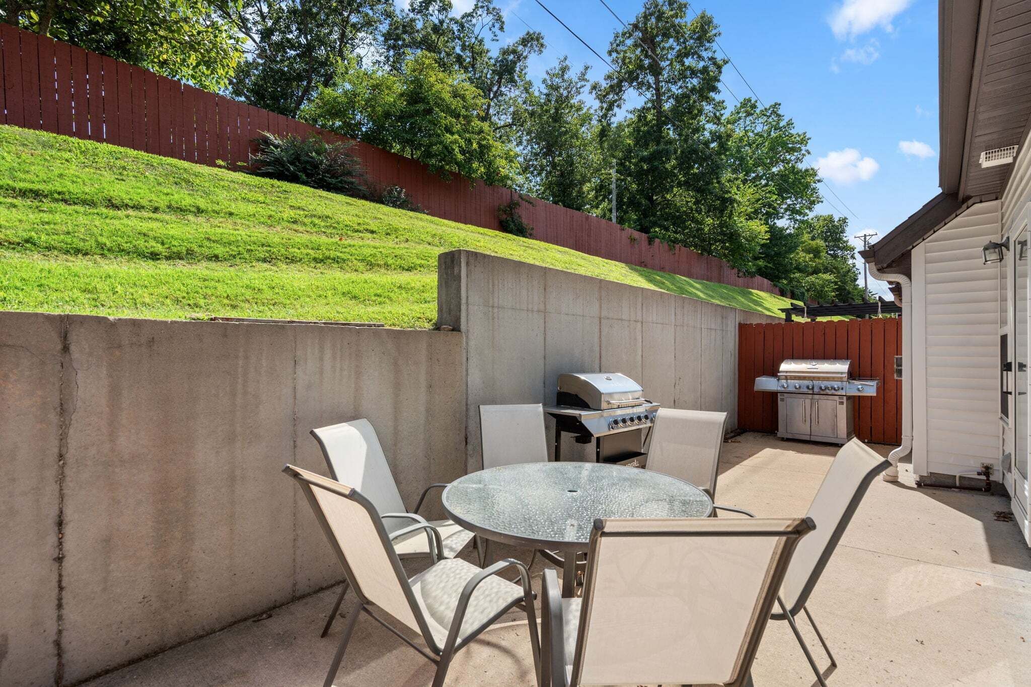 An outdoor patio with a grill, chairs, and a table.