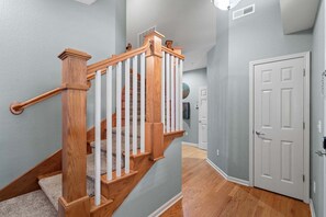 A wooden staircase with white balusters leading to a landing, a white door, and a hallway with grey walls and wooden flooring.