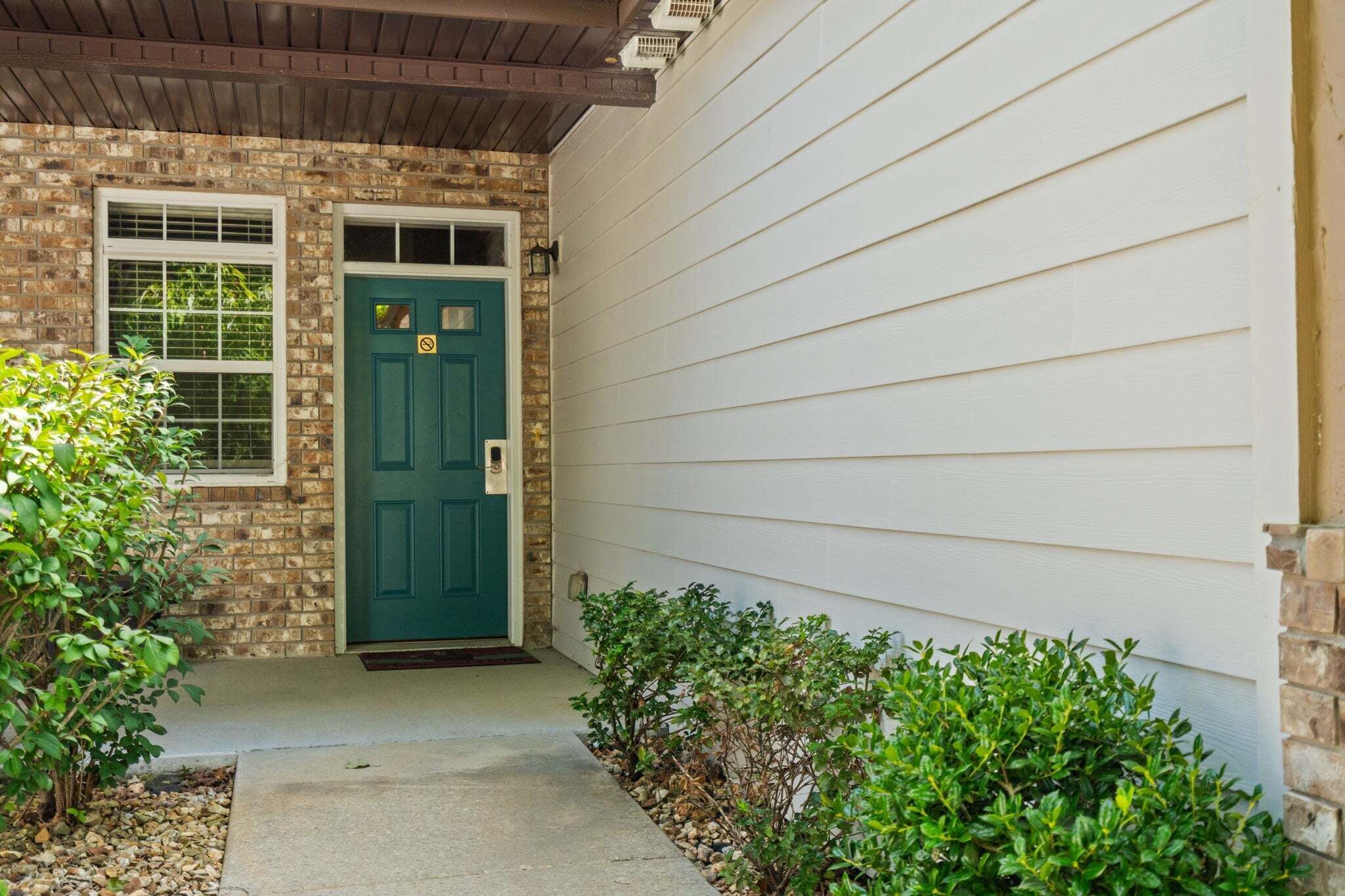 A house with a green door, a brick section, and a white siding exterior.