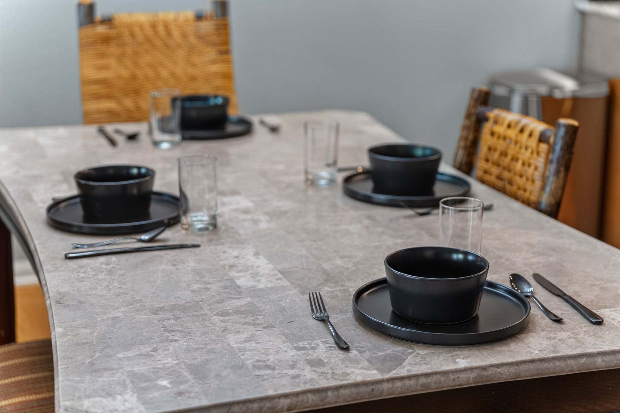 A dining table set with black plates, bowls, cutlery, and glasses.