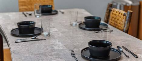 A dining table set with black plates, bowls, cutlery, and glasses.