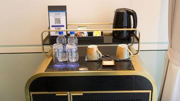 A hotel room's minibar with a coffee maker, water bottles, and a mug.