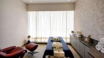 Relax in a serene spa room with a massage table, red massage chairs, and a vase of flowers.
