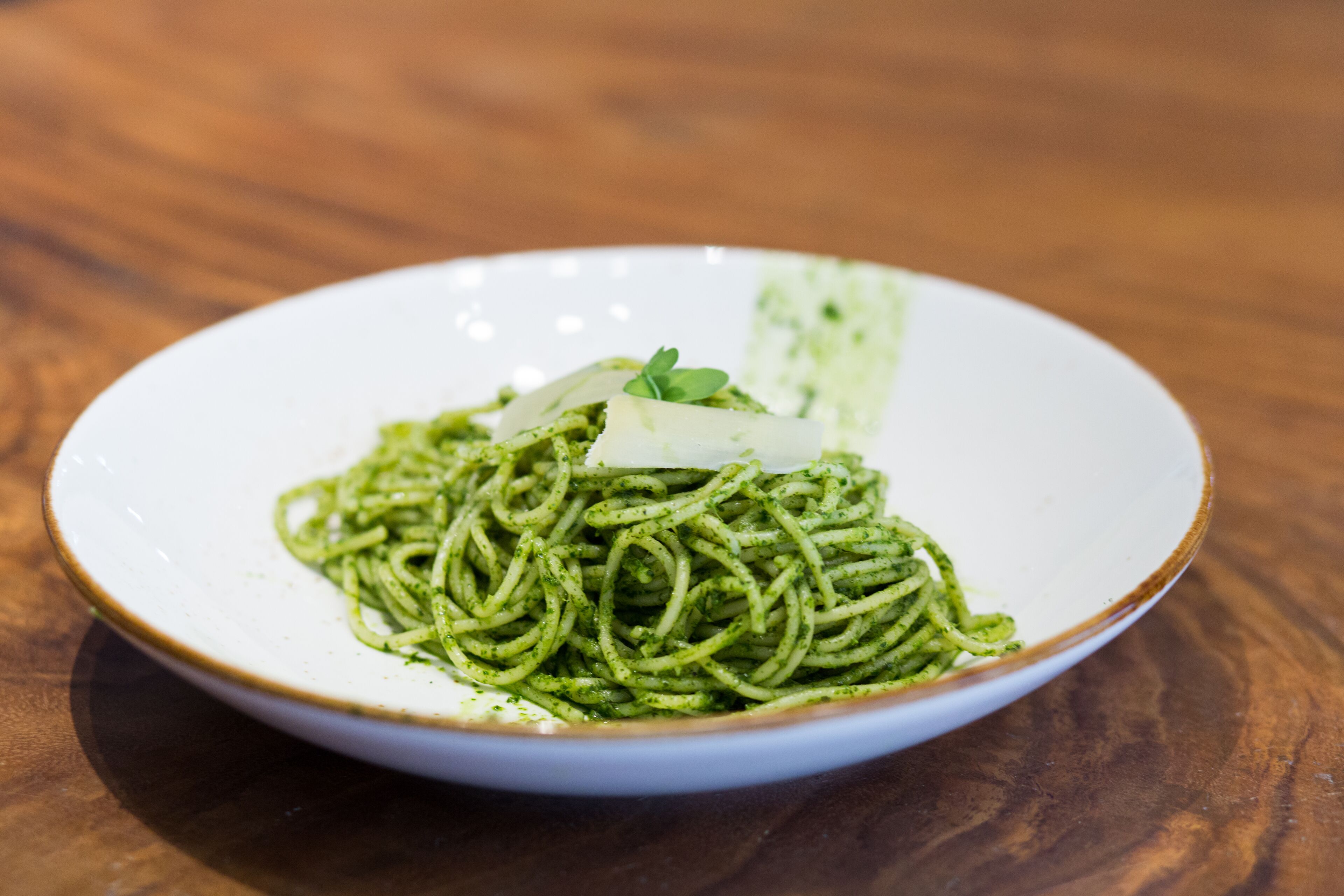 A plate of spaghetti with a green sauce and a slice of cheese on a white plate.